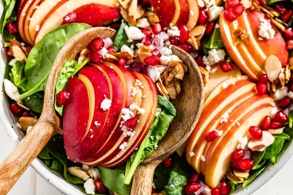 Close up view of Apple Spinach Salad with wood serving spoons scooping some out.
