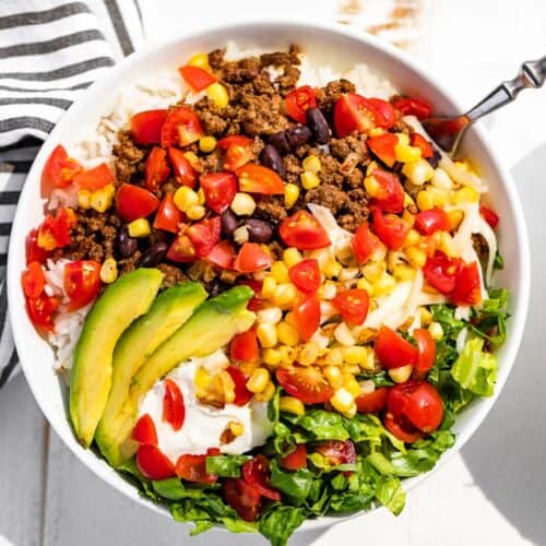 Straight down view of all the ingredients for taco bowls in two white bowls with a striped linen on the side.