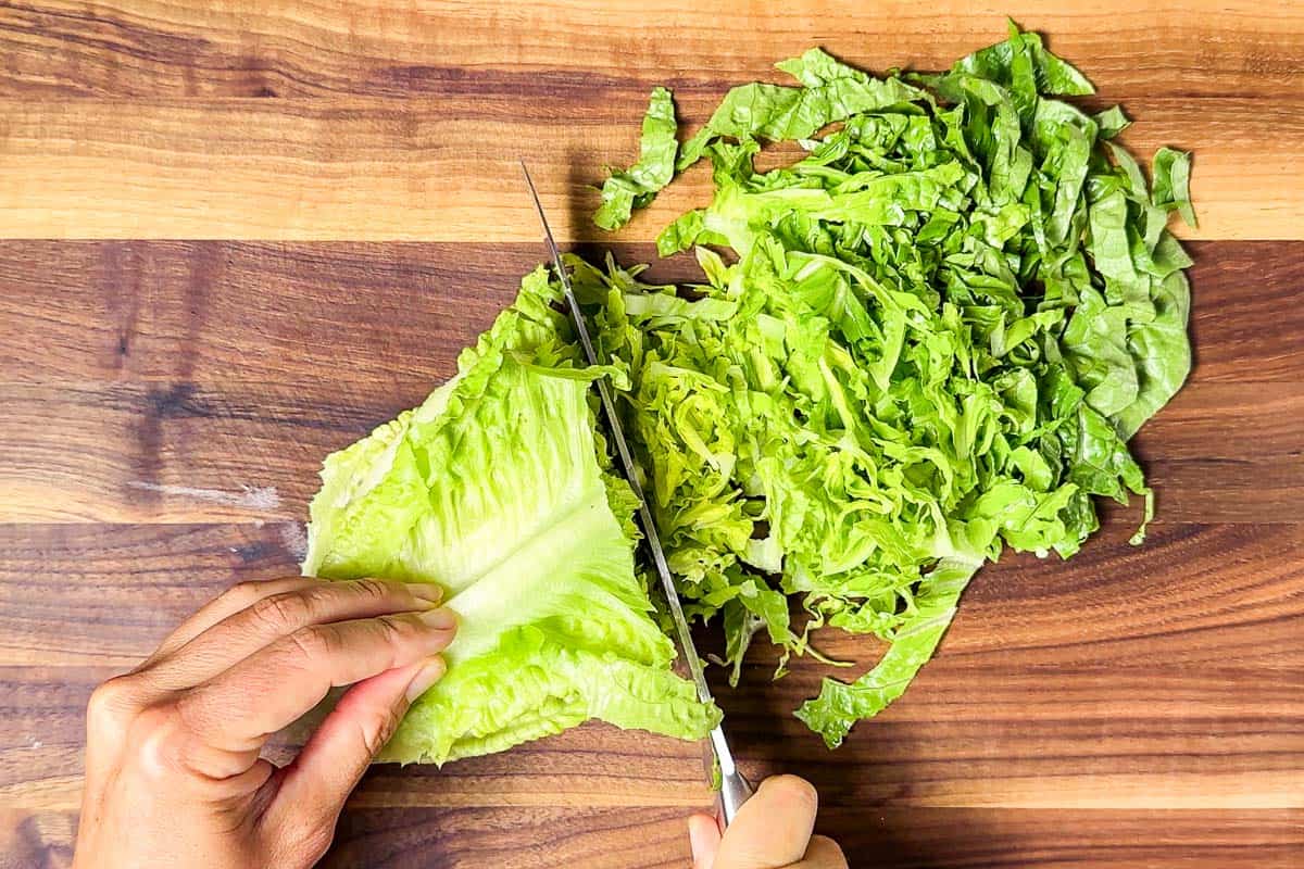 Cutting the romaine lettuce into shreds on a wood cutting board.