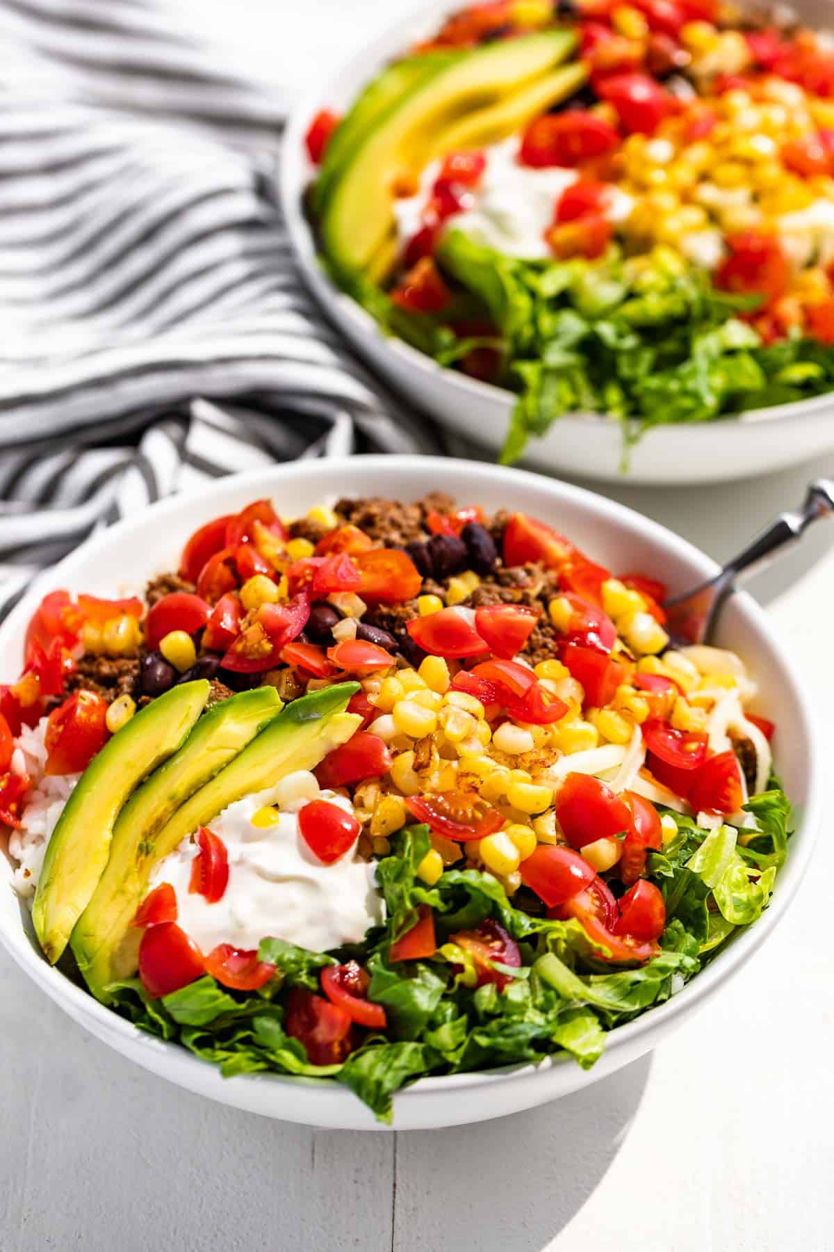 Side view of Taco Bowls topped with fresh tomatoes, corn, and avocado slices.