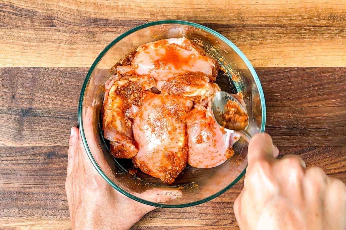 Combining the chicken thighs with the red curry paste marinade in a glass container.