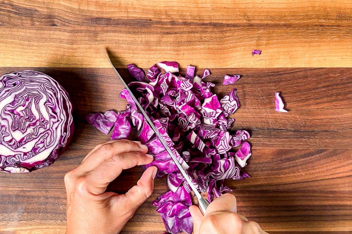 Chopping red cabbage on a wood cutting board with a large chef's knife.
