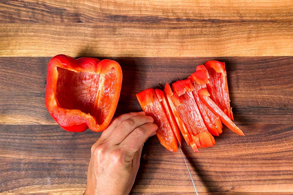 Slicing up a red bell pepper on a wood cutting board with a pairing knife.