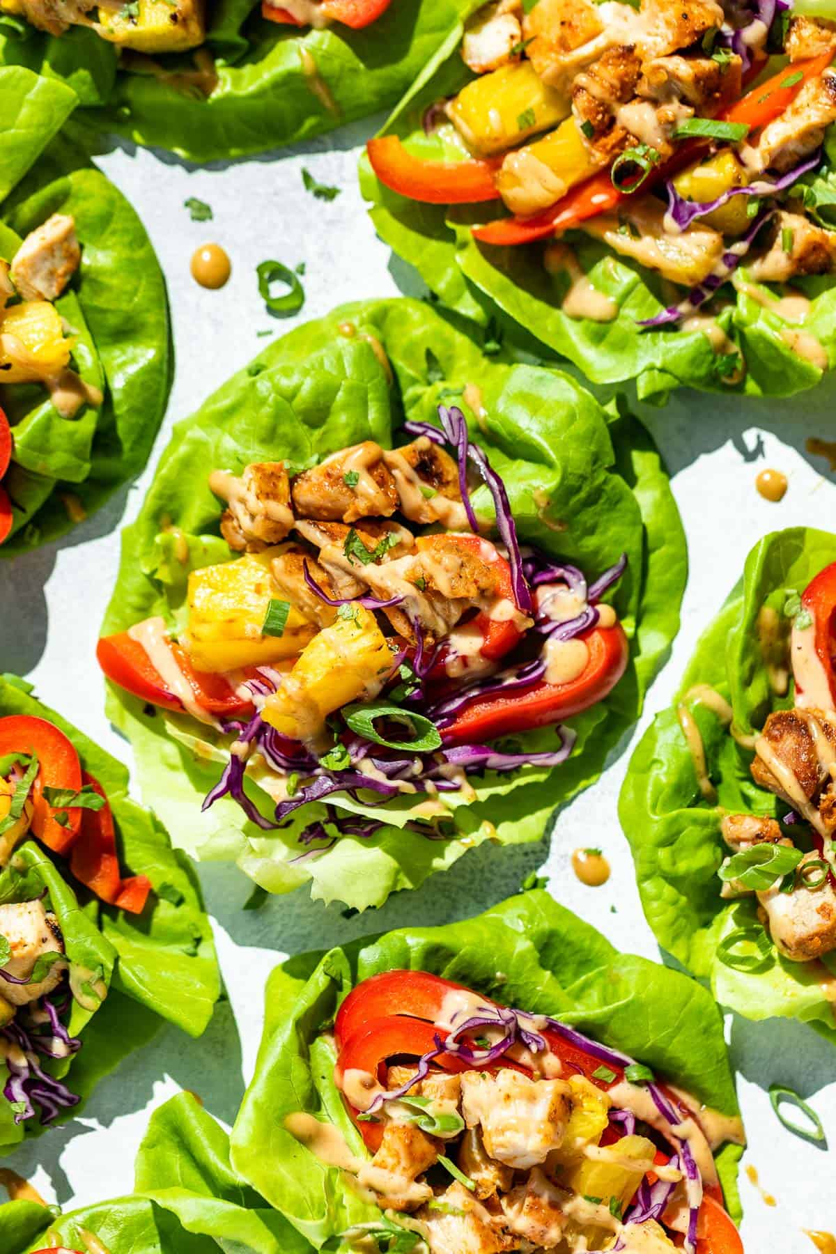 Seven Thai Lettuce Wraps placed on a blue background topped with peanut sauce and green onions.