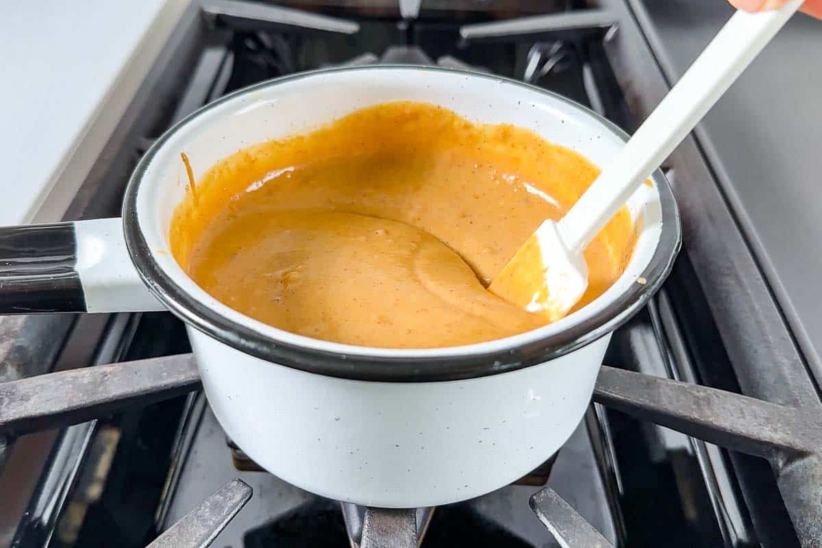 Stirring together the peanut sauce in a small white saucepan on the stove top.