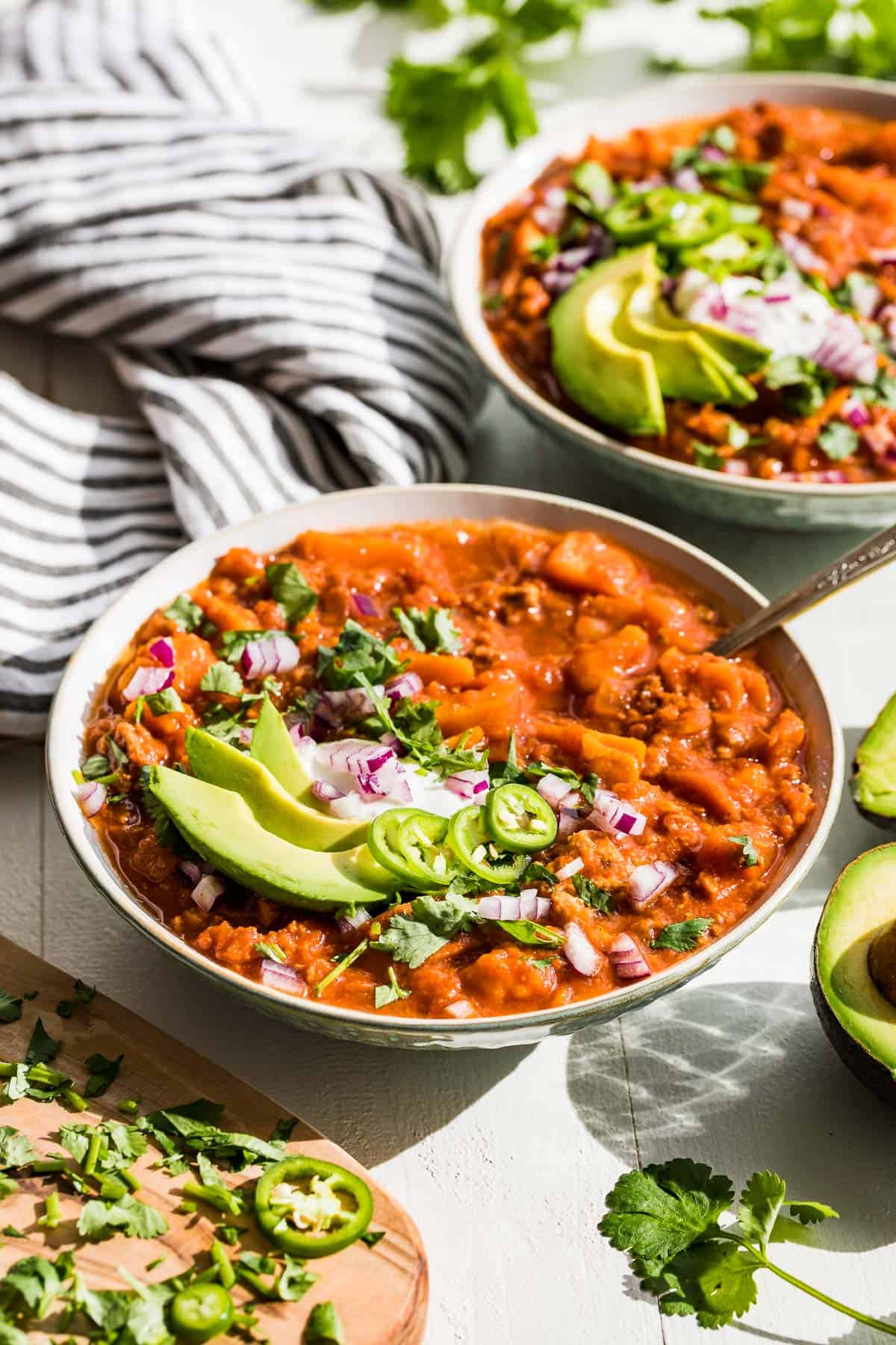 Side view of two bowls of Whole30 sweet potato turkey chili with all the toppings and avocado on the side.