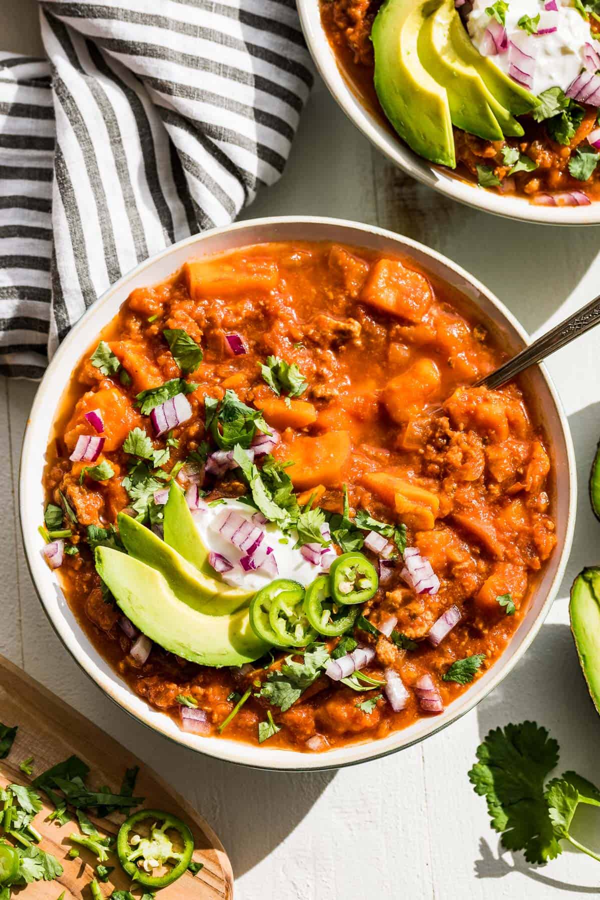 Close up straight down view of Whole30 turkey sweet potato chili in a bowl topped with avocado slices, cilantro, and red onion.