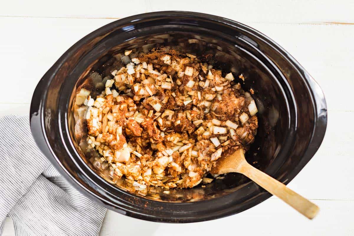 Mixing together the ground beef with the onions and chili spices in a slow cooker bowl.