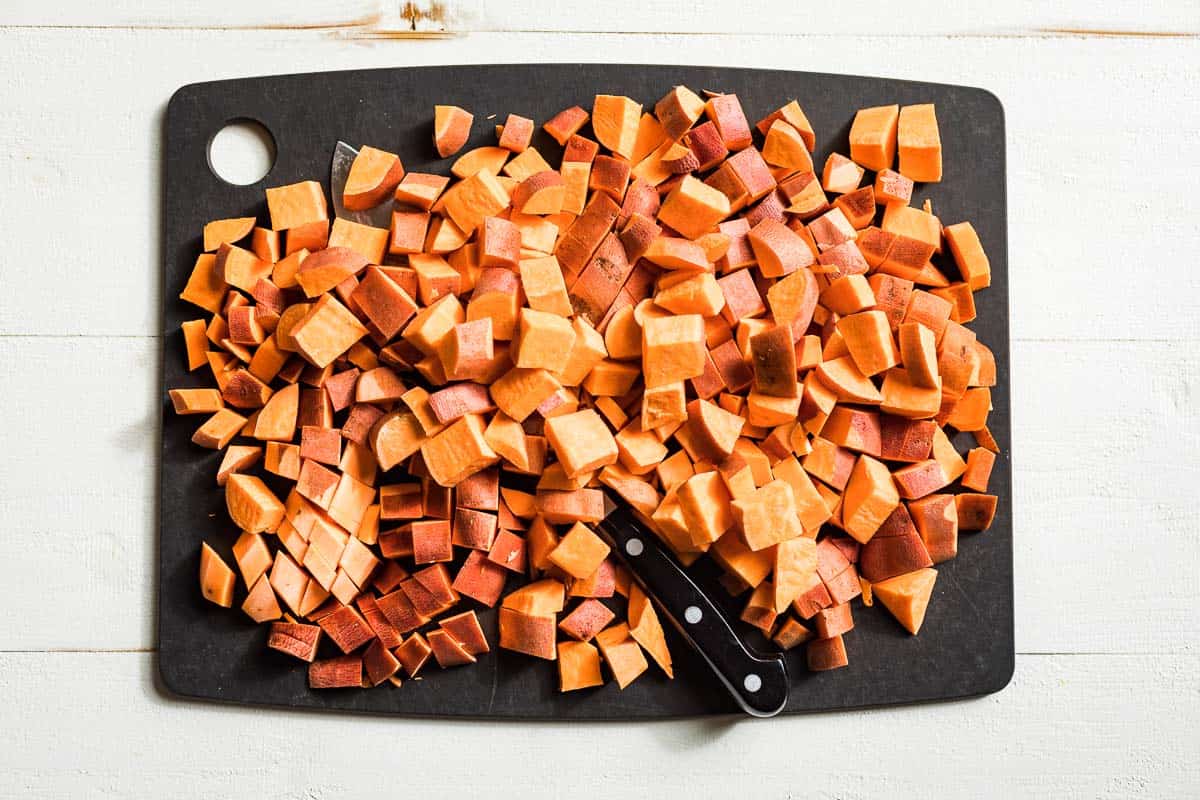Diced up sweet potato chunks on a black cutting board.