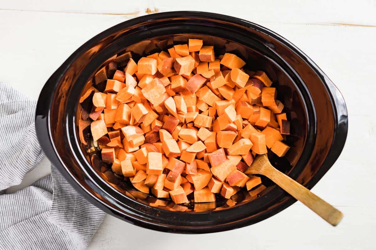 Adding the diced sweet potatoes to the slow cooker bowl.