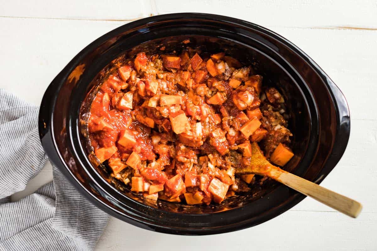 Mixing together the chili ingredients in the slow cooker bowl with a wood spoon.