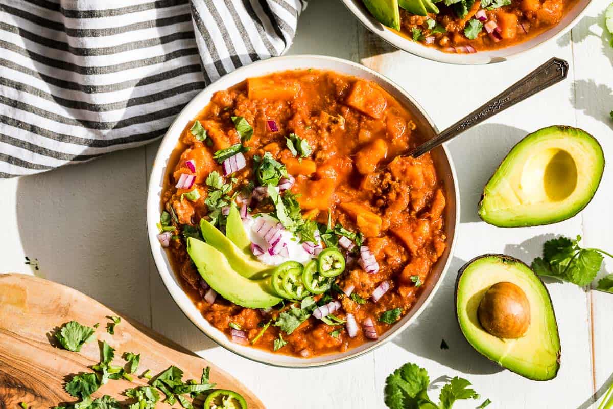 Straight down view of Whole30 Chili with all the toppings in a bowl with a havled avocado and cilantro on the side.