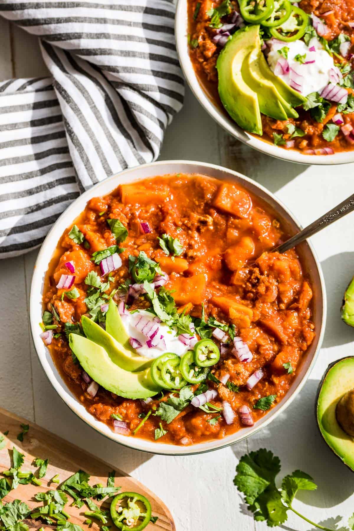 Straight down view of two bowls Whole30 sweet potato chili topped with avocado slices, cilantro, and jalapeno slice.