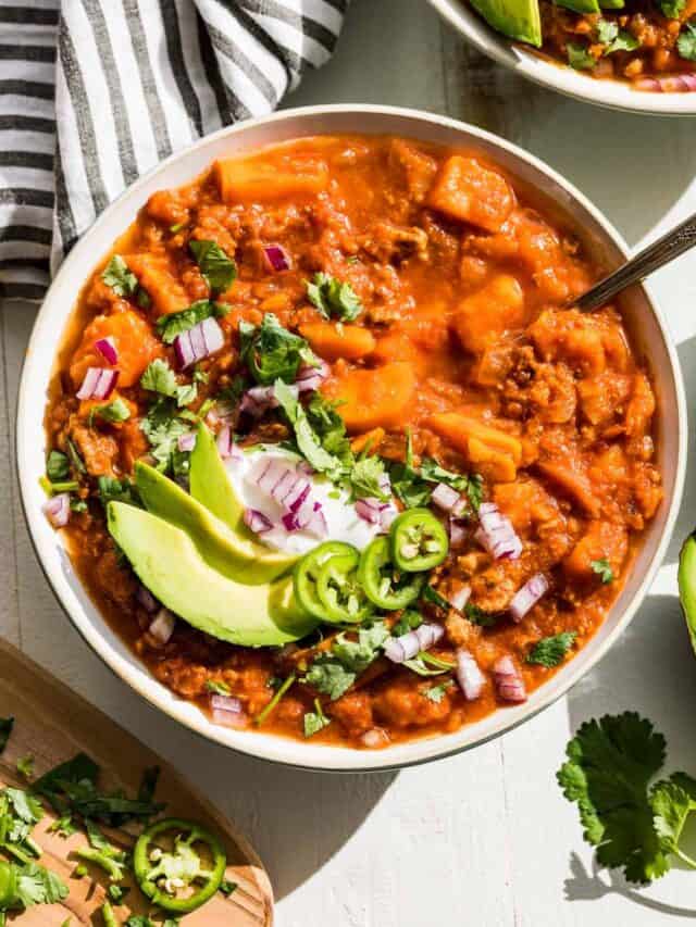 Close up straight down view of Whole30 turkey sweet potato chili in a bowl topped with avocado slices, cilantro, and red onion.