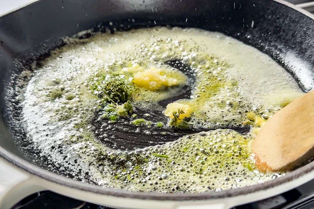 Sautéing the minced garlic and rosemary in melted butter in a large skillet with a wood spoon.