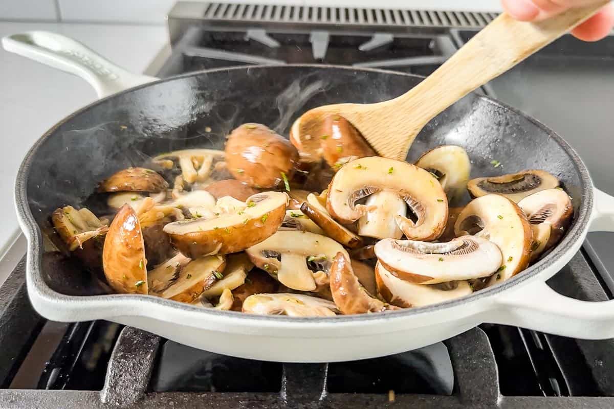 Sautéing the mushrooms in a large cast iron skillet with a wood spoon.