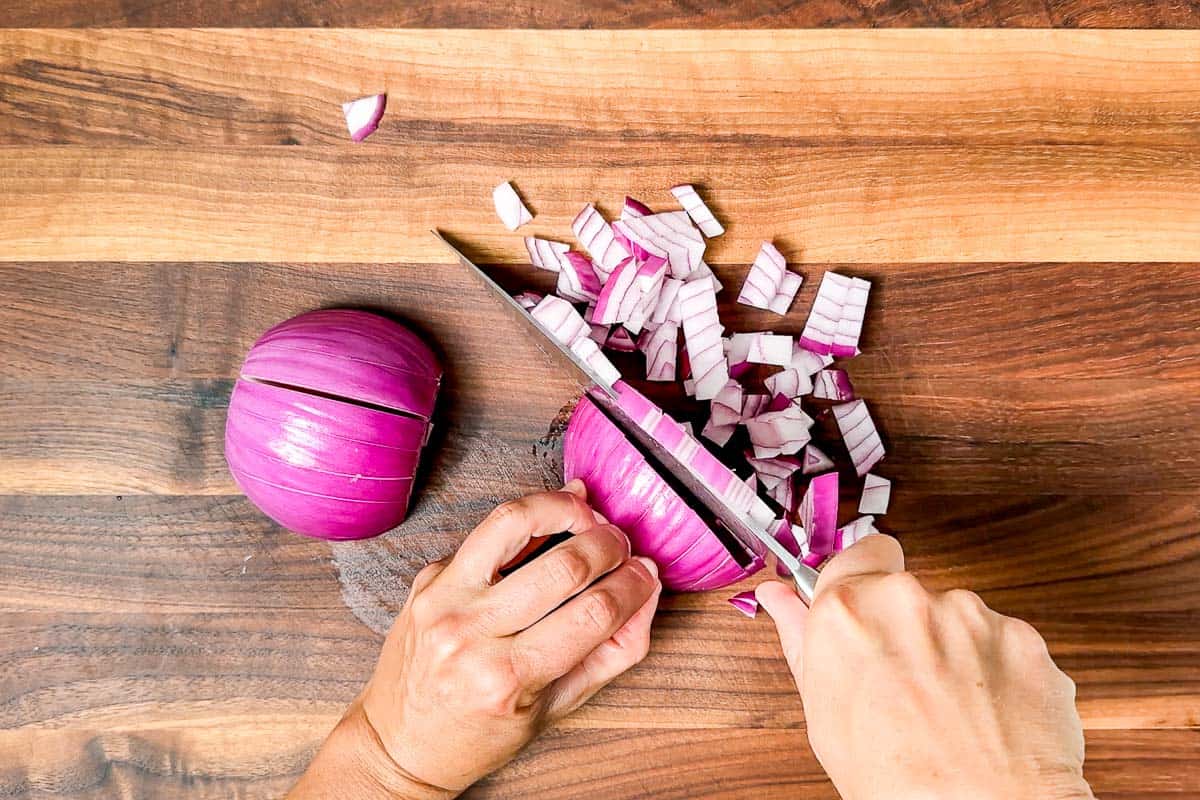 Dicing up a red onion with a chef's knife on a wood cutting board.