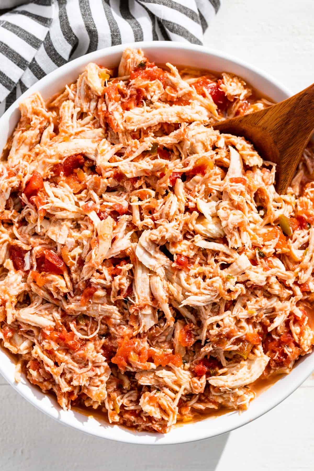 Close up view of shredded salsa chicken in a white bowl with a wood spoon in it.