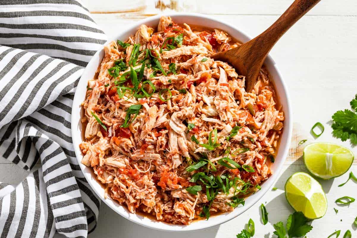 A large white bowl filled with shredded salsa chicken topped with green onions and cilantro.