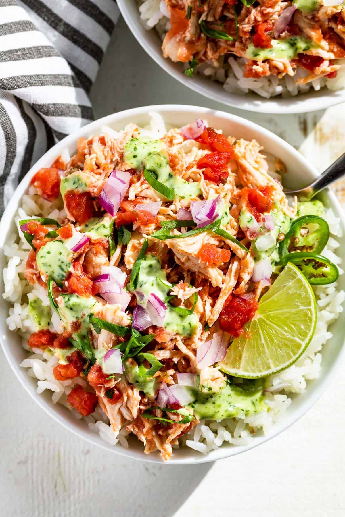 Two bowls filled with rice topped with salsa chicken, salsa, and cilantro lime dressing.