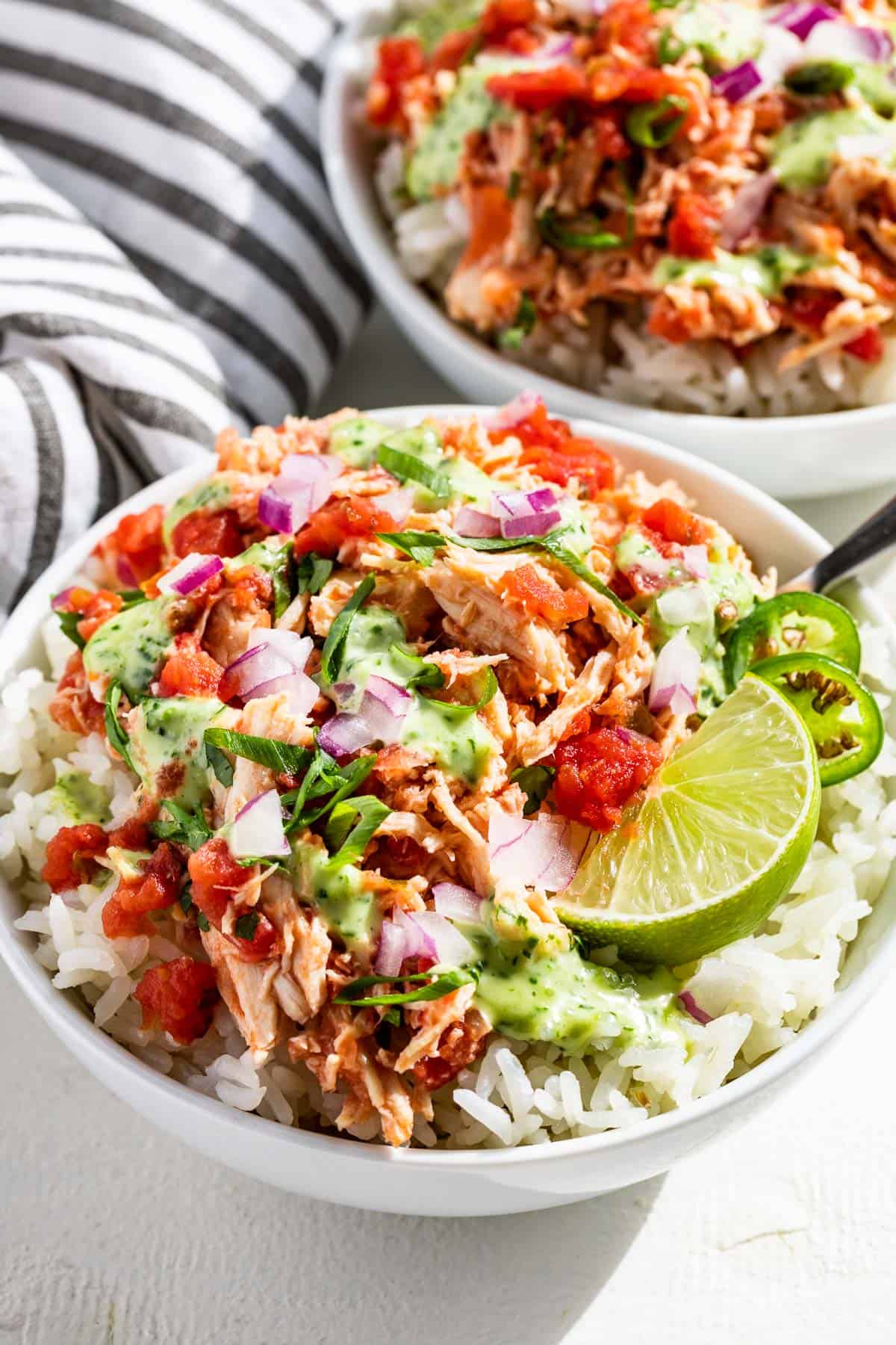 Two bowls of rice topped with salsa chicken, salsa, cilantro lime dressing, and a lime wedge.