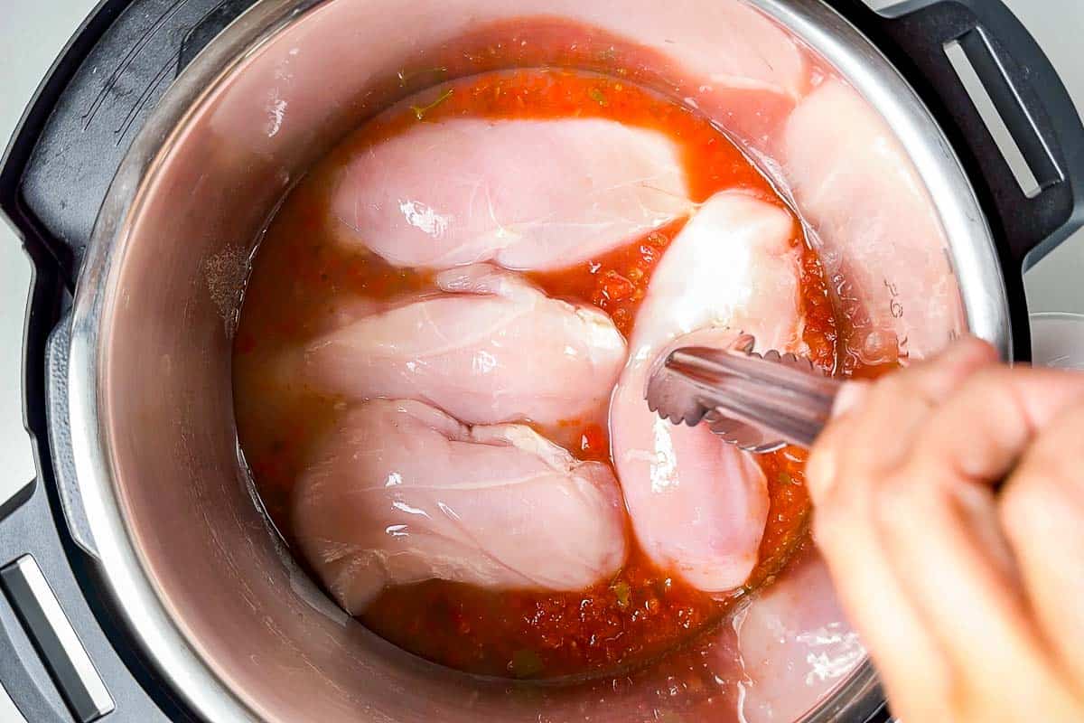 Adding the chicken breasts to the salsa broth mixture in an Instant Pot cooking bowl.