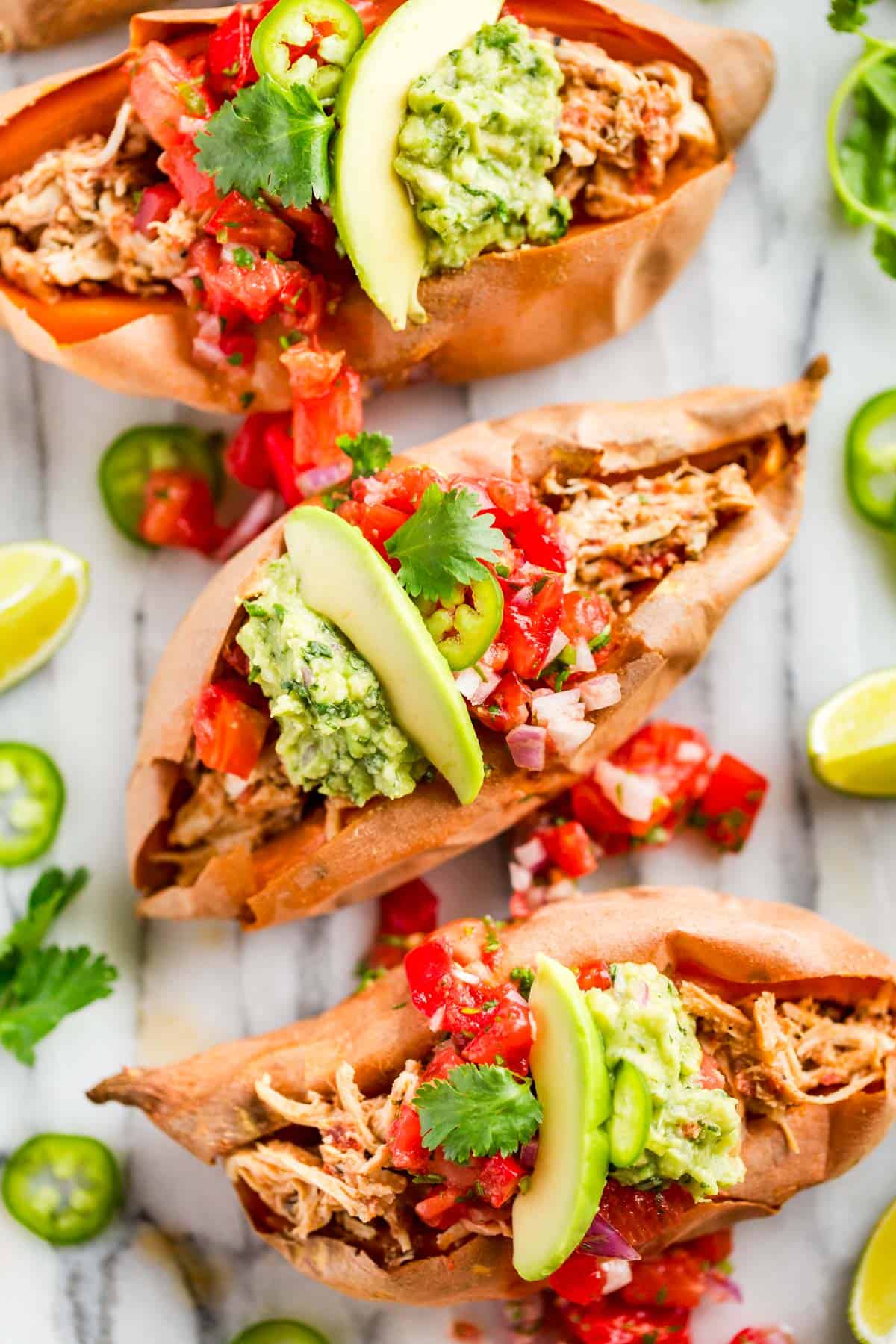 Shredded salsa chicken piled into baked sweet potatoes topped with salsa and sliced avocado.