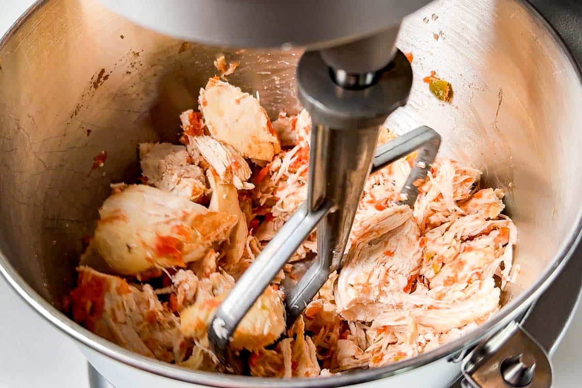 Shredding the salsa chicken in an electric mixer bowl with the paddle attachment.