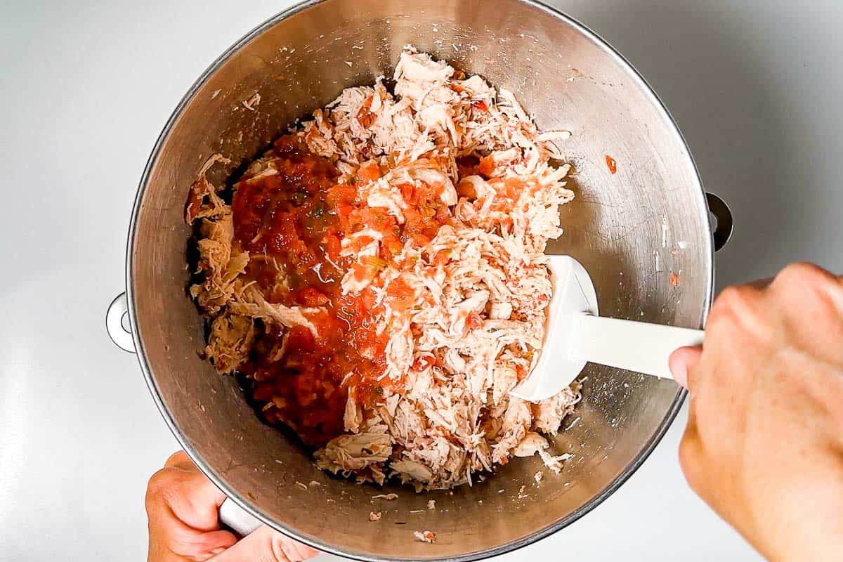 Adding more salsa to the shredded chicken in a metal mixing bowl.