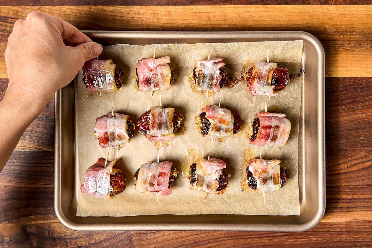 Turning the half cooked bacon wrapped dates on the baking sheet.