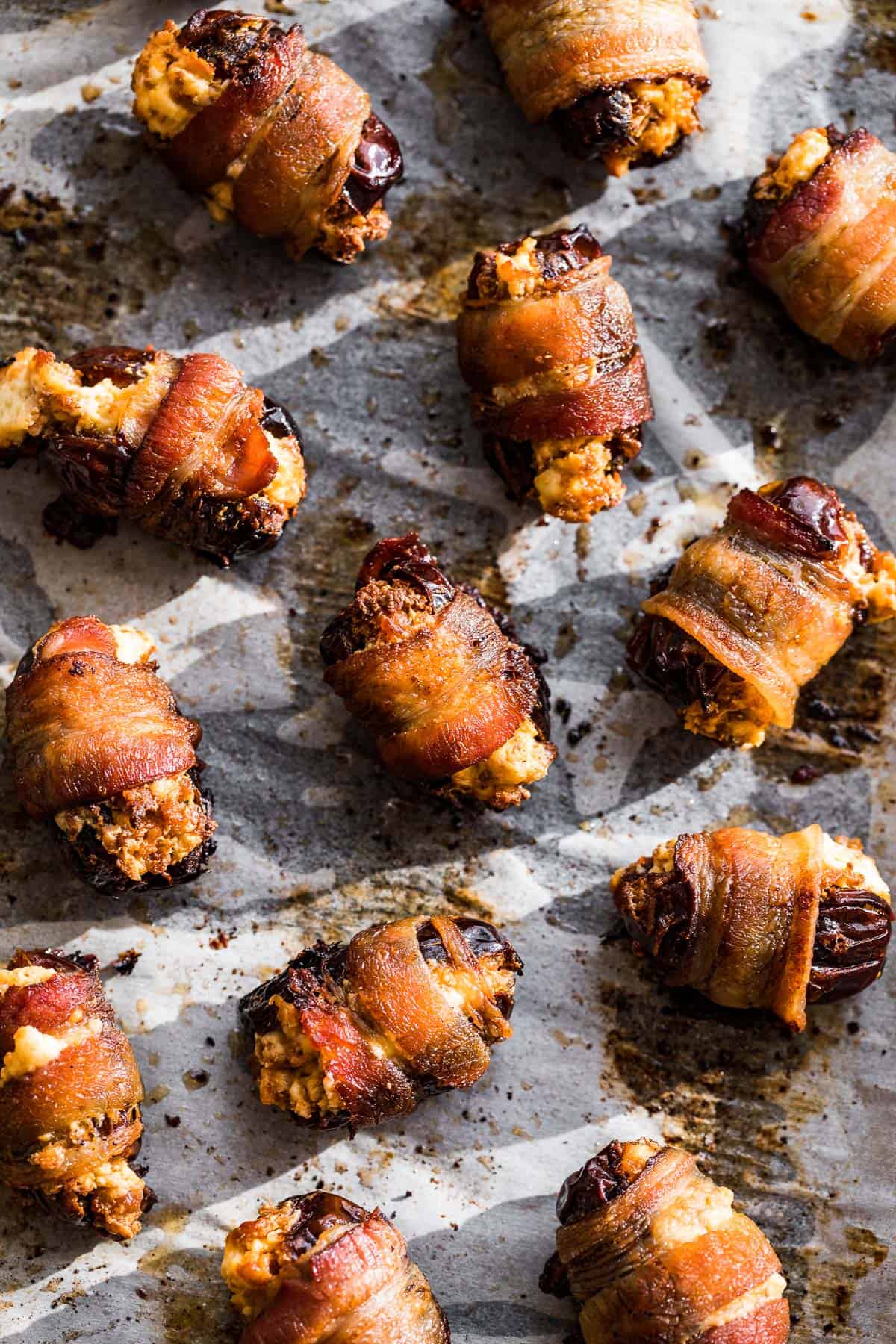 Thirteen bacon wrapped dates on white parchment paper.