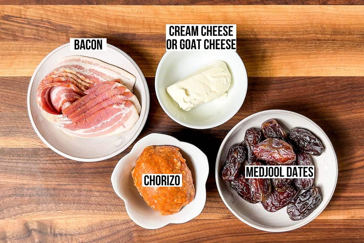 Medjool dates, thinly sliced bacon, chorizo sausage, and cream cheese in pottery bowls on a wood cutting board.