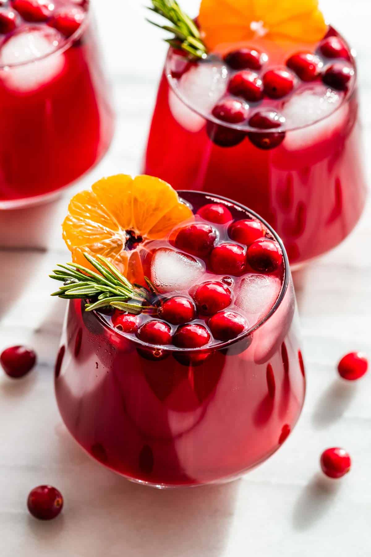 Cranberry kombucha mocktails in clear glasses topped with fresh cranberries, sliced oranges and rosemary sprigs.