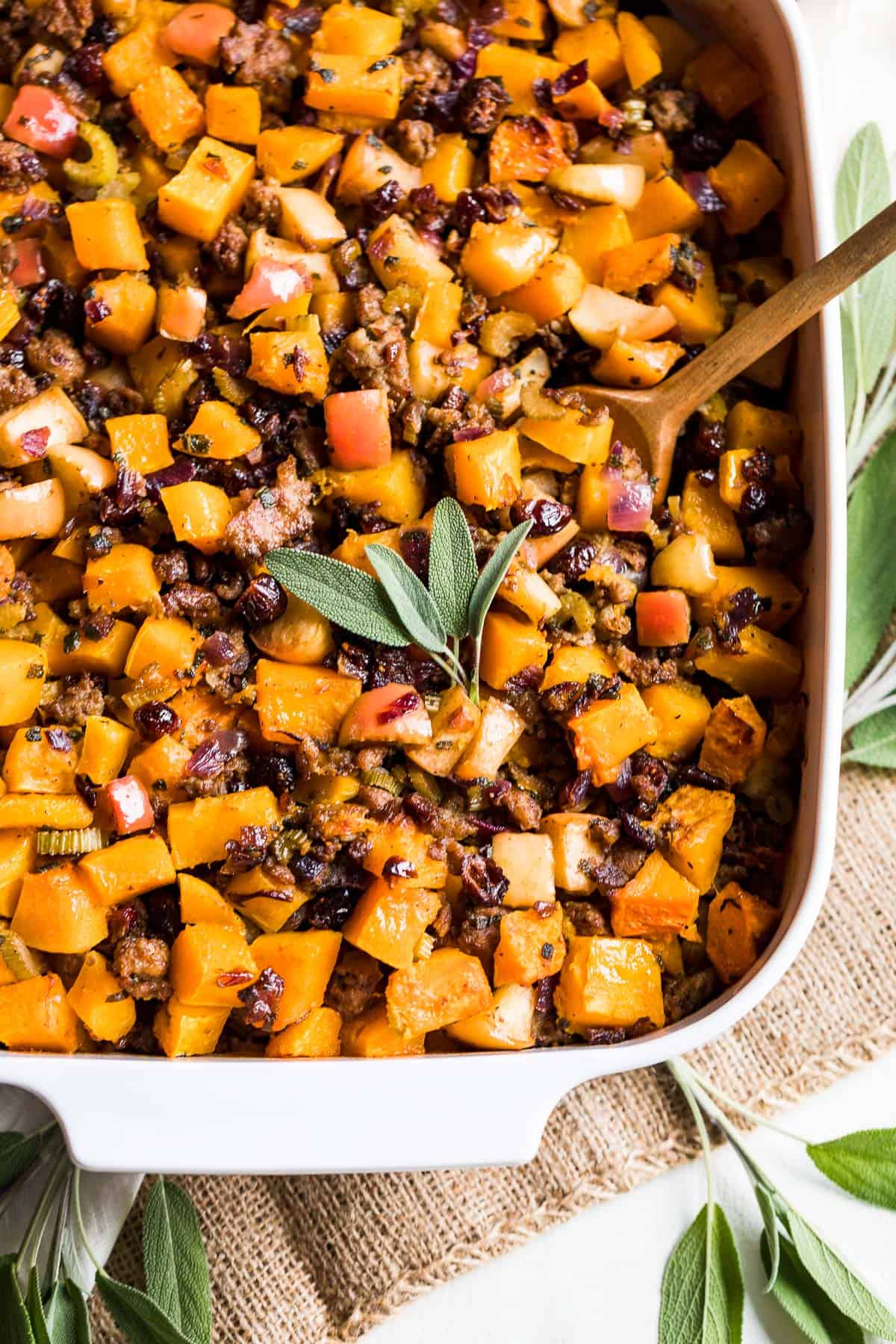 A white baking pan filled with Butternut Squash Paleo Stuffing topped with fresh sage leaves.