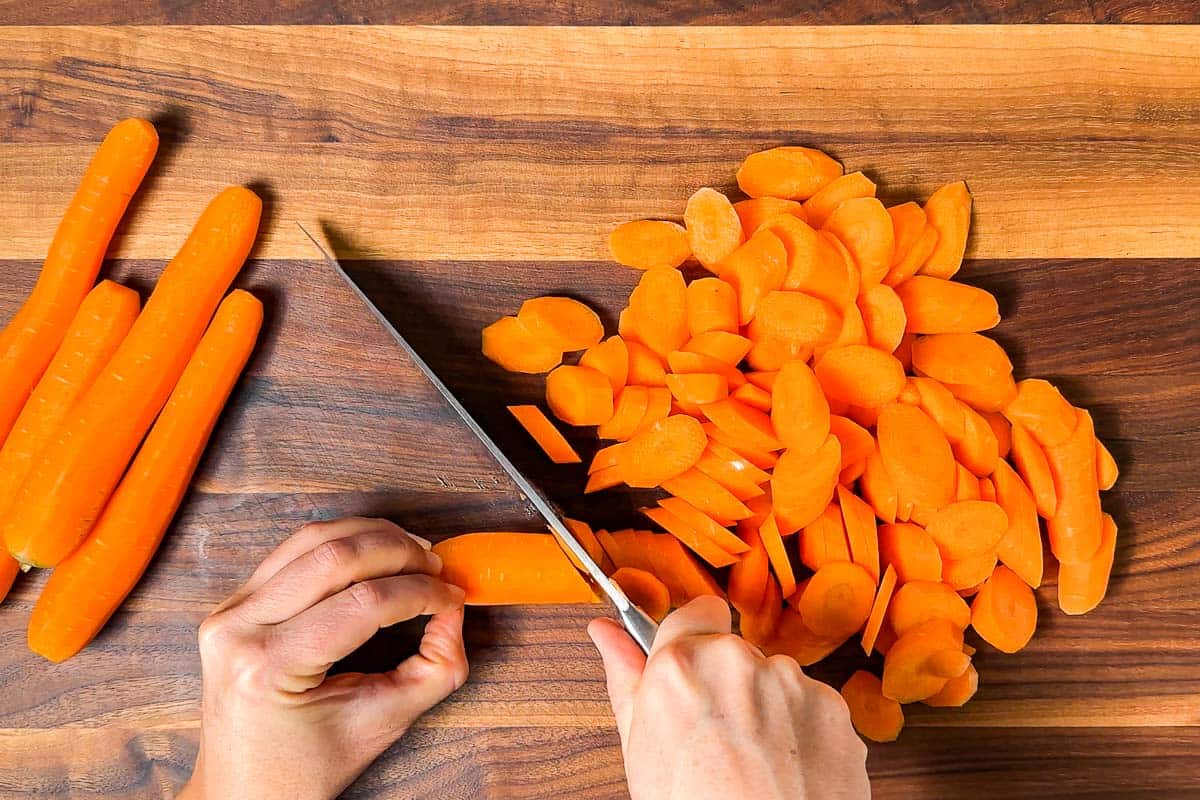 Slicing the carrots on a wood cutting board with a chefs knife.