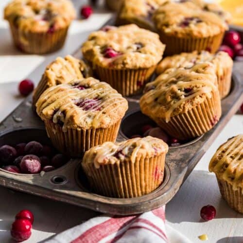 Finished Paleo Cranberry Orange Muffins in an antique muffin tin with muffins, orange slices and cranberries around the tin.