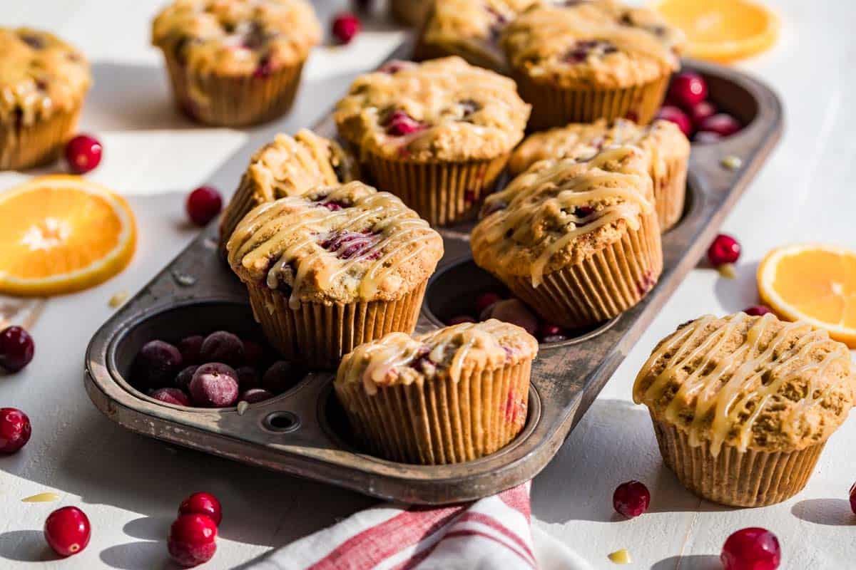 Finished Paleo Cranberry Orange Muffins in an antique muffin tin with muffins, orange slices and cranberries around the tin.