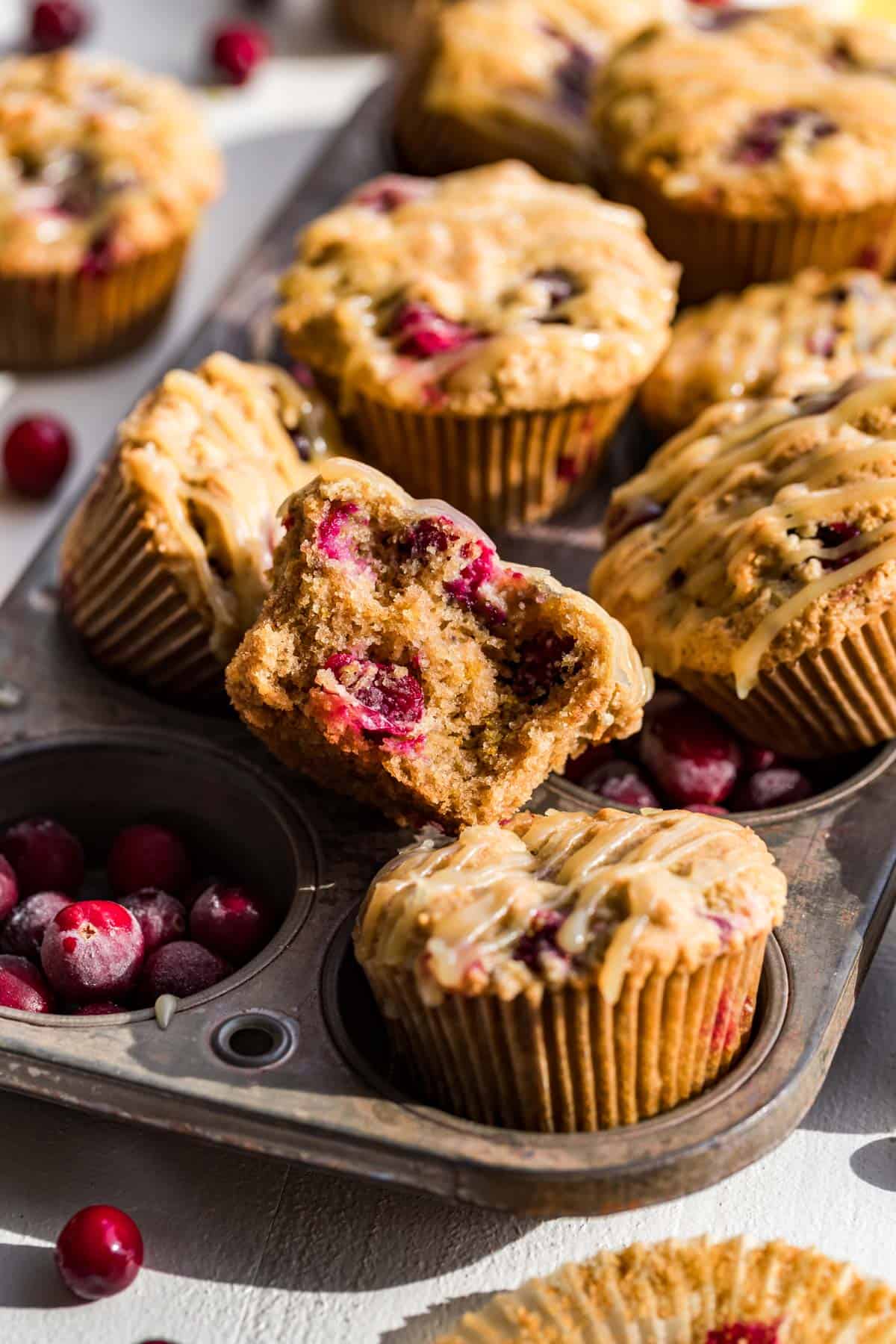 Cranberry Orange Muffins in an antique muffin tin with one muffin broken open showing the fluffy texture.