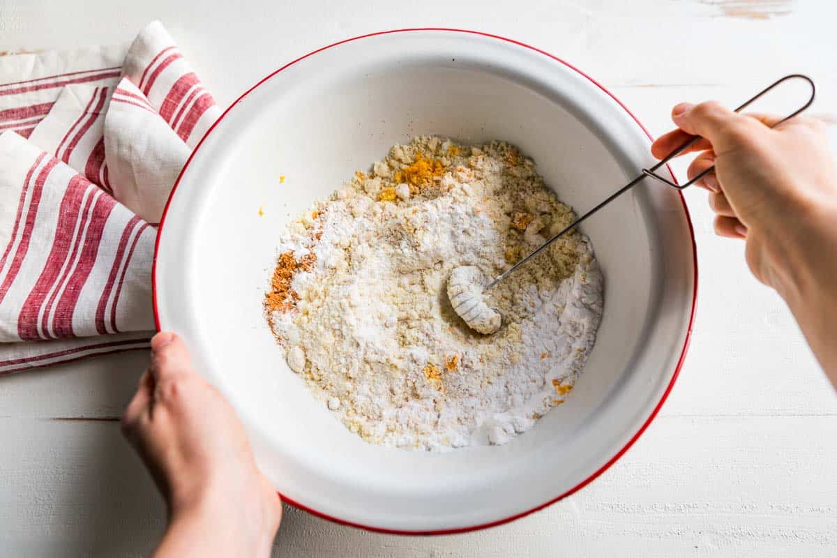 Whisking together the flour dry ingredients in a red rimmed white bowl.