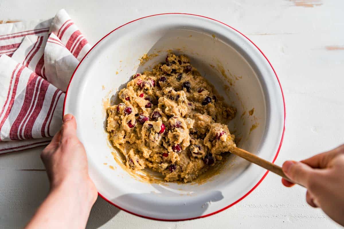 Fully mixed cranberry orange muffin batter in a red rimmed white bowl.