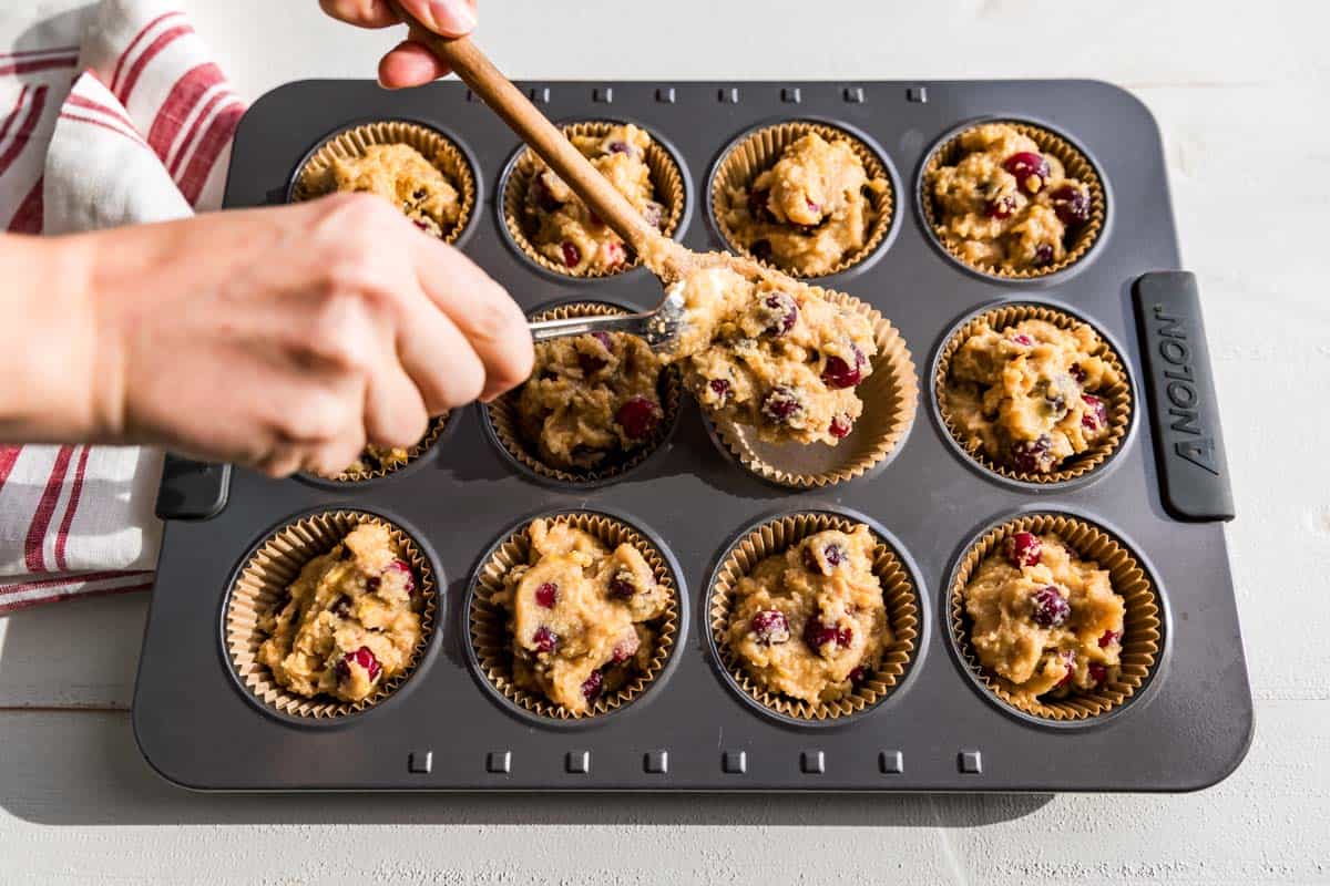Portioning the cranberry orange muffin batter into a muffin tin with two spoons.