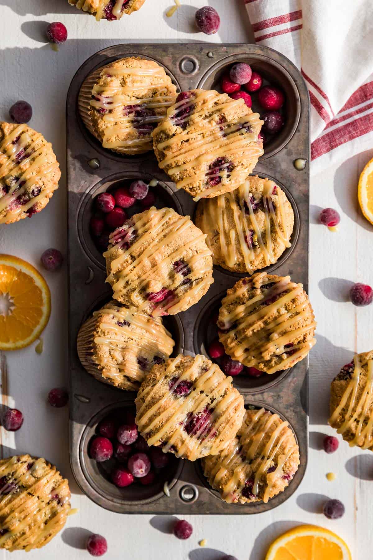 Cranberry Orange Muffins in an antique muffin tin with orange slices and cranberries around it.