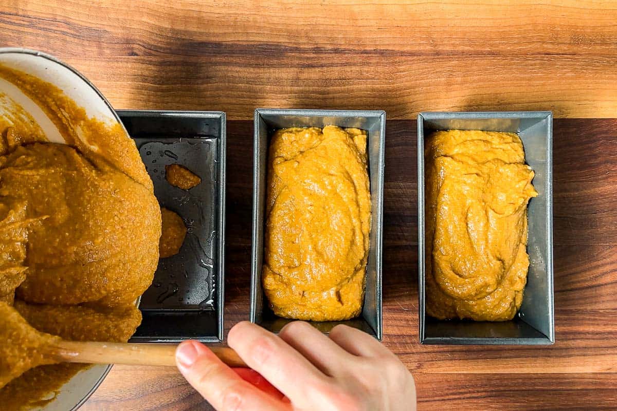 Portioning out the pumpkin bread batter into mini loaf pans on a wood cutting board.