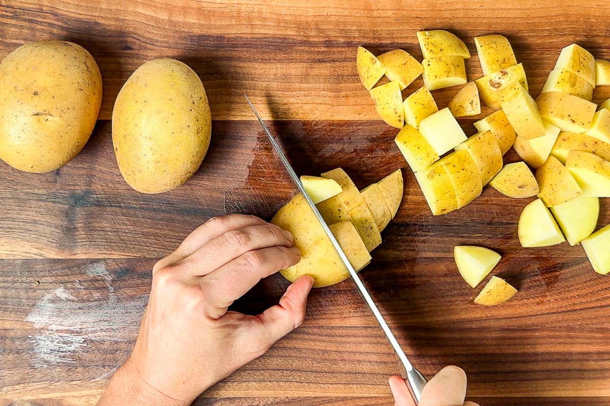 Cutting up the potatoes on a wood cutting board with a chefs knife.