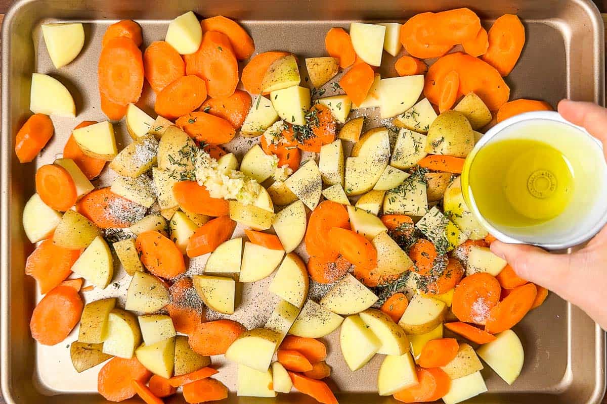 Adding the potatoes, carrots, chopped herbs, and olive oil to a baking sheet.