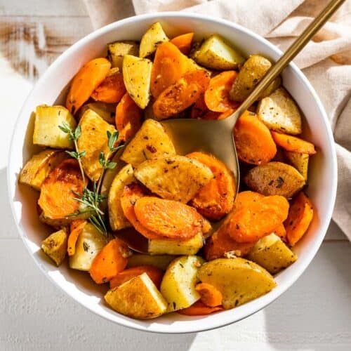 Roasted Potatoes and Carrots in a white bowl with a gold spoon.