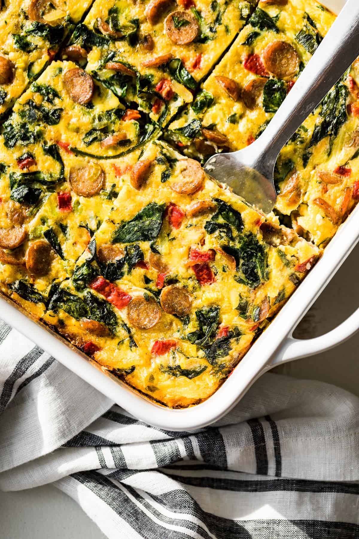 A slice of sausage hash brown breakfast casserole being lifted out of the baking dish with a metal spatula.