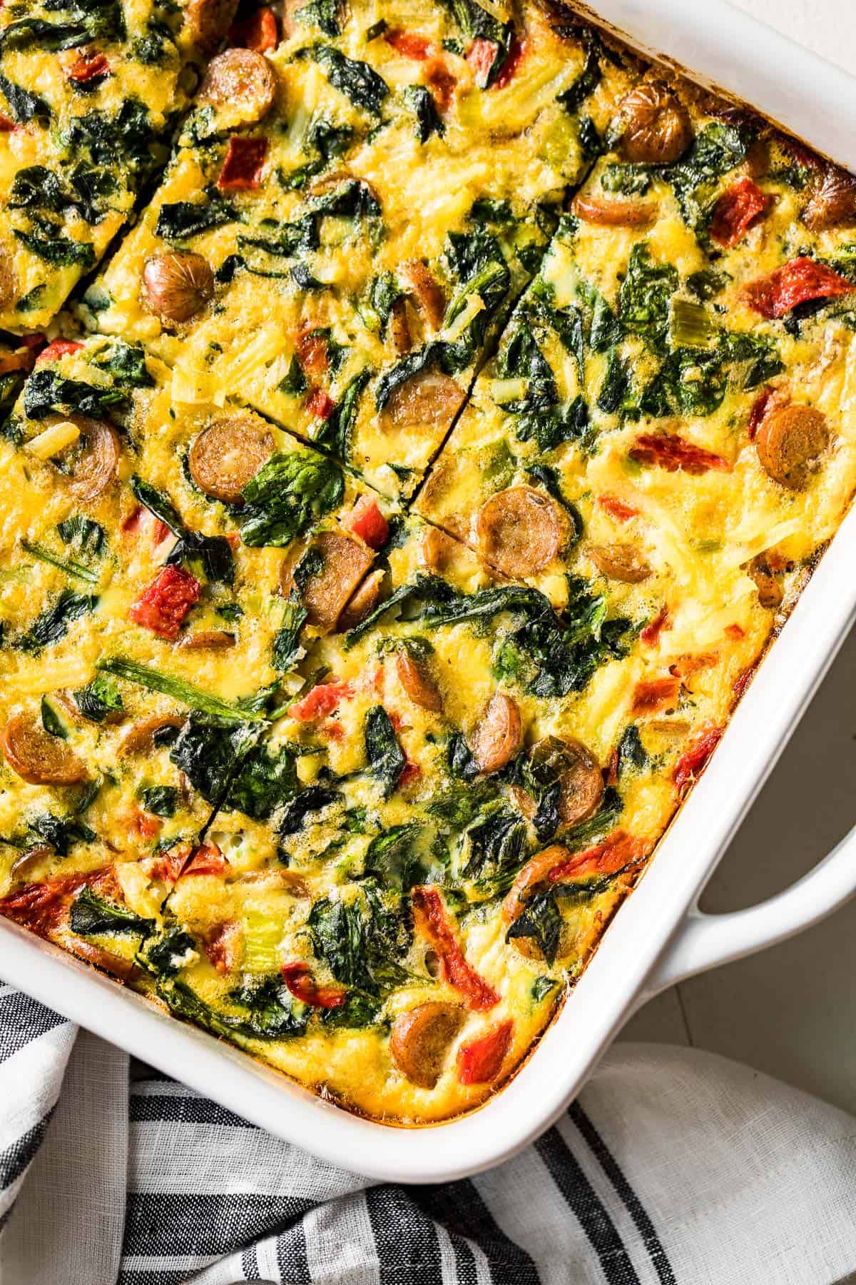 Sliced breakfast casserole in a large white baking dish with a blue and white striped linen on the side of the dish.