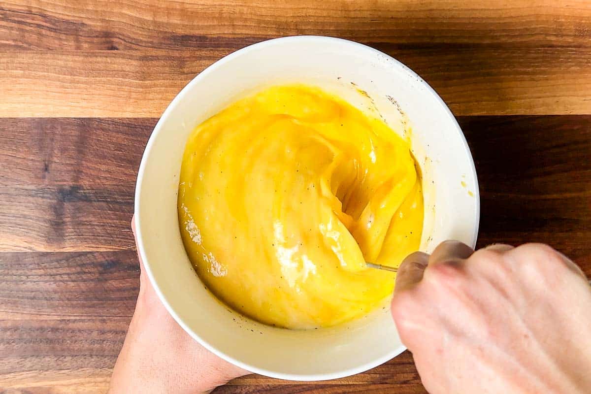 Whisking together the eggs with milk in a white bowl with a whisk.