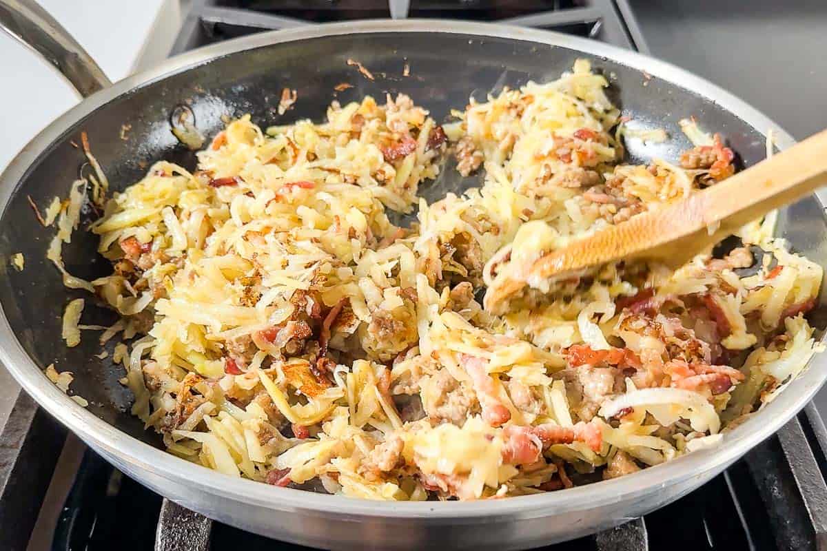 Cooking the hash browns together with the sausage and bacon in a skillet on the stove.